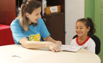 Rede Municipal de Criciúma inicia ano letivo com novidades Professora e aluna sorriem durante atividade pedagógica em sala de aula da rede municipal de Criciúma, representando o acolhimento e a preparação para o início do ano letivo de 2026.