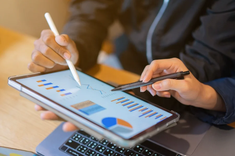 Close de mãos analisando gráficos e estatísticas de negócios na tela de um tablet, ilustrando o levantamento do Sebrae/SC sobre o perfil e a renda dos empreendedores catarinenses.