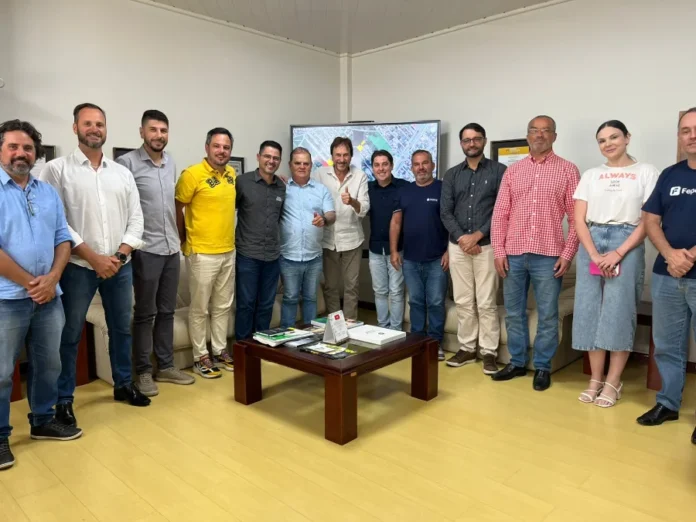 Representantes da Baly visitam Araranguá para novo complexo Representantes da Baly Brasil e da Prefeitura de Araranguá posam para foto oficial em gabinete. Ao centro, o prefeito Cesar Cesa faz um sinal de positivo. No fundo, um monitor exibe um mapa aéreo detalhado da área onde será construído o novo parque fabril.