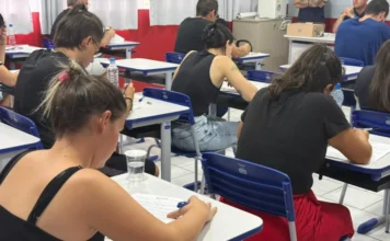 SAMAE Araranguá divulga classificação de processo seletivo Uma sala de aula com várias pessoas sentadas em carteiras escolares, vistas de costas, realizando a prova escrita do processo seletivo simplificado do SAMAE de Araranguá.