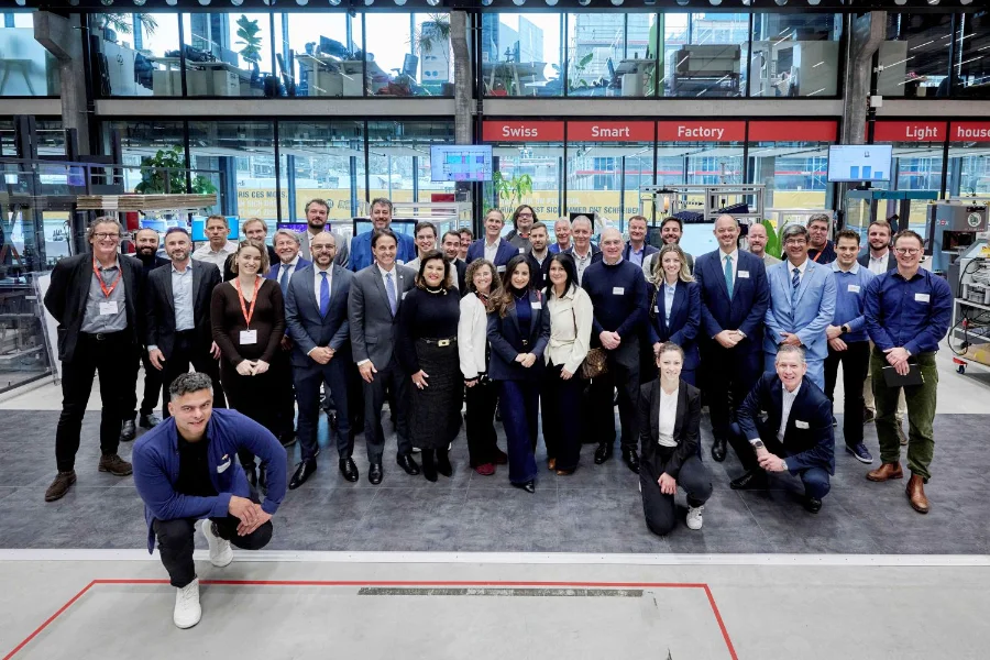 Membros da comitiva oficial de Santa Catarina, liderada pela vice-governadora Marilisa Boehm, posam para foto em grupo ao lado de empresários e autoridades suíças no interior da Swiss Smart Factory. O ambiente é amplo e tecnológico, com paredes de vidro e equipamentos industriais ao fundo, simbolizando a cooperação em inovação e tecnologia entre o Estado e o Cantão de Berna.