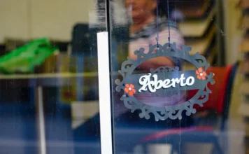 SC bate recorde com saldo de 140 mil novas empresas em 2025 Placa decorativa com a palavra "Aberto" pendurada na porta de vidro de um estabelecimento comercial, simbolizando o recorde de abertura de empresas e novos negócios em Santa Catarina em 2025.