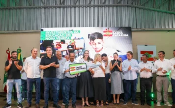 SC investe R$ 11,7 milhões em escolas no Sul do estado O governador Jorginho Mello, ao lado da secretária da Educação Luciane Ceretta e outras autoridades, segura uma chave simbólica grande durante evento em Nova Veneza. Ao fundo, um telão exibe a frase "Investimentos da Educação em Nova Veneza