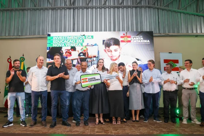 SC investe R$ 11,7 milhões em escolas no Sul do estado O governador Jorginho Mello, ao lado da secretária da Educação Luciane Ceretta e outras autoridades, segura uma chave simbólica grande durante evento em Nova Veneza. Ao fundo, um telão exibe a frase "Investimentos da Educação em Nova Veneza