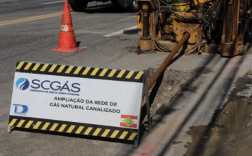 SCGÁS investirá R$ 104,8 milhões em Santa Catarina em 2026 Canteiro de obras em via pública com uma placa de sinalização da SCGÁS indicando "Ampliação da rede de gás natural canalizado". Ao fundo, um equipamento de perfuração insere a tubulação no solo, ilustrando os investimentos em infraestrutura urbana mencionados na matéria.