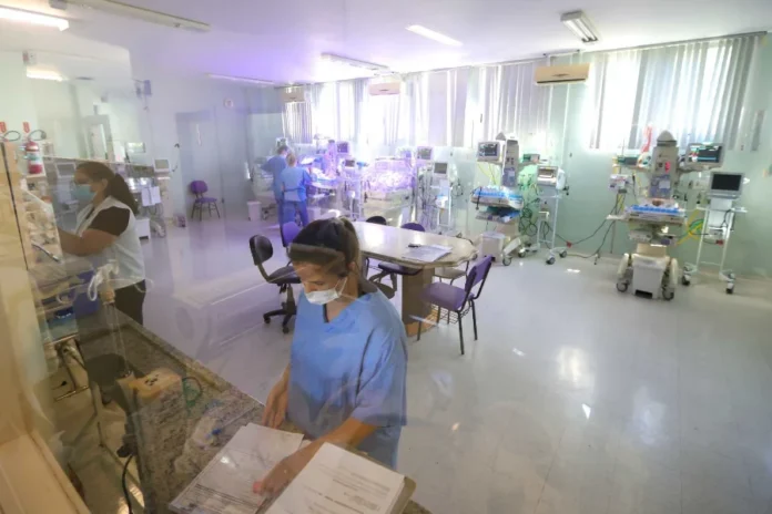 SES SC 70 mil disputam concurso da saúde neste domingo Profissionais de saúde, usando máscaras e uniformes, trabalham em uma Unidade de Terapia Intensiva Neonatal (UTI neonatal) equipada com incubadoras e monitores.