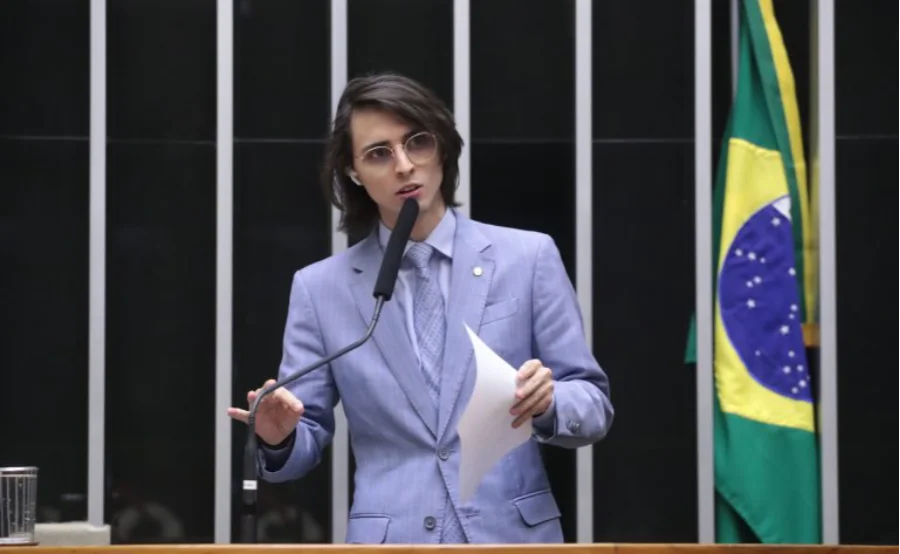 O deputado federal Amom Mandel (Cidadania-AM), de terno azul e óculos, discursa no púlpito da Câmara dos Deputados, segurando papéis. Ele foi o relator do projeto que aprovou regras para o fornecimento de medicamentos para autismo pelo SUS.