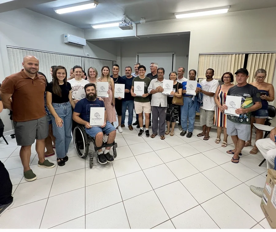 Santa Rosa do Sul entrega 73 novas escrituras pelo Reurb Foto em grupo realizada no auditório da Prefeitura de Santa Rosa do Sul, mostrando cerca de 20 pessoas, entre moradores e autoridades, reunidas para a entrega de escrituras do Reurb. Diversos participantes aparecem sorridentes e seguram pastas brancas com o logotipo da empresa