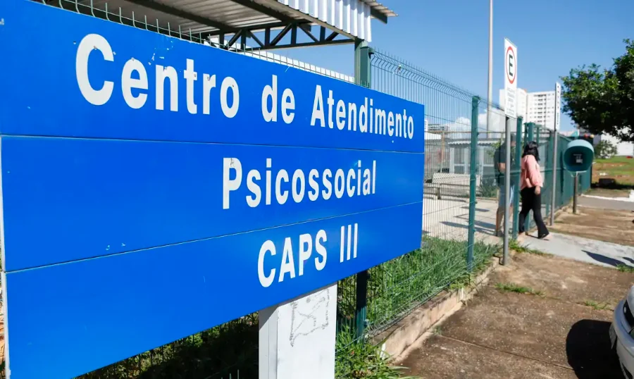 Placa azul de identificação de um Centro de Atendimento Psicossocial (CAPS III) em primeiro plano. Ao fundo, vê-se a estrutura externa da unidade de saúde sob um céu claro. A imagem ilustra a Rede de Atenção Psicossocial (Raps), cujas normas de financiamento e diretrizes estão sendo revisadas pelo Ministério da Saúde.