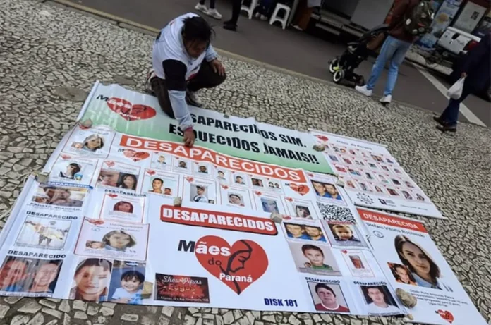 Senado analisa criação de delegacias de desaparecidos Mulher ajoelhada em uma calçada de mosaico português ao lado de banners e diversos cartazes espalhados com fotos e nomes de pessoas desaparecidas. Um dos banners centrais exibe o logotipo do grupo Mães do Paraná — um coração vermelho com a silhueta de um rosto feminino — acompanhado da frase "Desaparecidos sim. Esquecidos jamais!". O registro ilustra a mobilização social que fundamentou a criação do projeto de lei para delegacias especializadas.