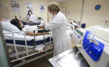 Senado analisa projeto com metas para Dia da Diálise Profissional de saúde supervisiona paciente durante sessão de diálise em ambiente hospitalar, com equipamento médico ao lado.
