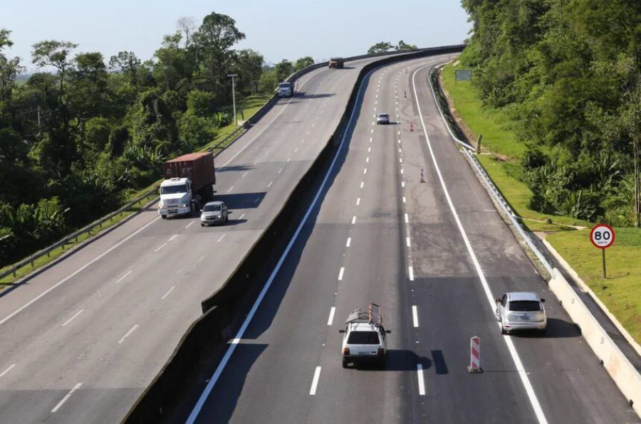 Vista panorâmica de uma rodovia de pista dupla com fluxo de carros e caminhões, cercada por faixas de domínio com vegetação verde e árvores, áreas que são foco do projeto de lei em pauta no Senado para autorização de atividades agrícolas.