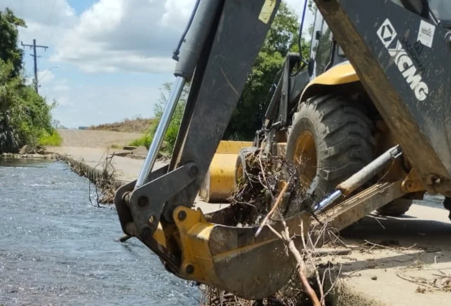 Uma retroescavadeira da Prefeitura de Turvo utiliza sua caçamba para retirar galhos e entulhos acumulados em uma ponte baixa na localidade de São Felipe. A ação visa desobstruir o leito do rio para prevenir alagamentos e garantir a segurança dos moradores durante períodos de chuvas intensas.