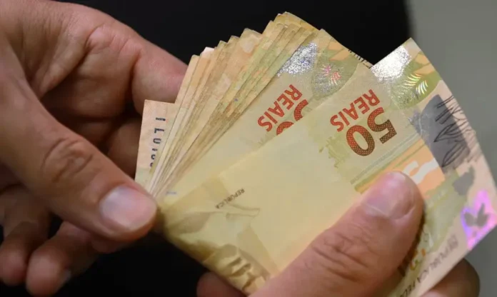 Valor do seguro-desemprego é reajustado em 3,9% em 2026 Mãos contam notas de cinquenta reais, ilustrando o pagamento do seguro-desemprego com os valores reajustados.