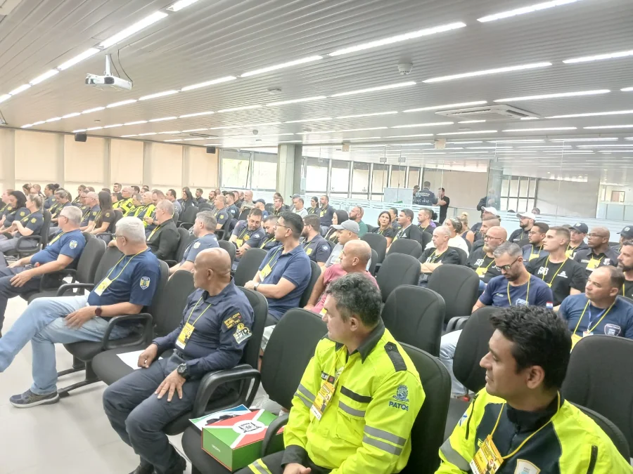 Fotografia em ângulo aberto de um auditório repleto de agentes de trânsito uniformizados, sentados em poltronas pretas, acompanhando as atividades do encontro estadual em Criciúma.