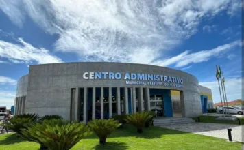 Arroio do Silva abre vagas de estágio para estudantes Fachada externa do Centro Administrativo Municipal Prefeito José Élio Borges, em Balneário Arroio do Silva. O edifício possui arquitetura moderna em concreto aparente com formato circular, pilares verticais e grandes janelas de vidro. À frente, há um jardim gramado com palmeiras baixas ornamentais sob um céu azul com nuvens esparsas. A imagem representa a sede da prefeitura onde serão alocados os novos estagiários selecionados pelo edital 001/2026.