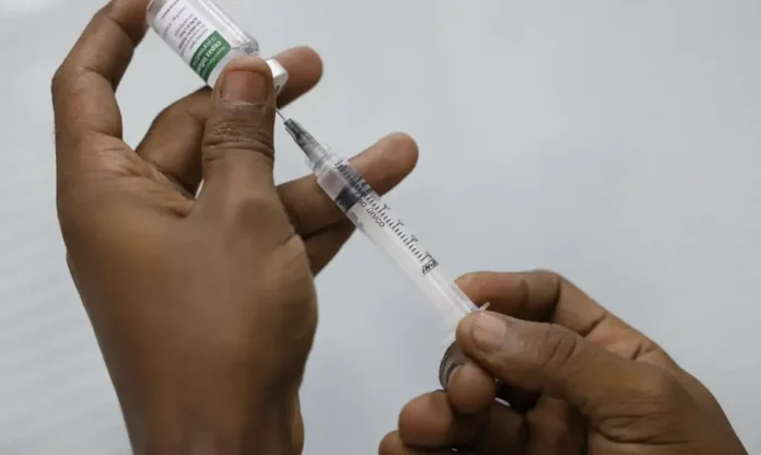 Brasil registra 29 mortes por Covid-19 no início do ano (1) Mãos de uma pessoa preparando uma vacina, com uma seringa e um frasco, ilustrando o processo de imunização contra a Covid-19 e outras doenças respiratórias, tema central da matéria sobre a importância da vacinação e a baixa adesão no Brasil.