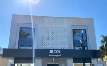 CDL Araranguá se posiciona contra novo feriado em SC Fachada frontal da sede da Câmara de Dirigentes Lojistas (CDL) de Araranguá, em Santa Catarina. O prédio de arquitetura moderna apresenta janelas espelhadas e uma placa preta centralizada com o logotipo da entidade em letras brancas. A imagem ilustra a instituição que lidera o movimento de preocupação com os impactos econômicos do novo projeto de lei estadual.