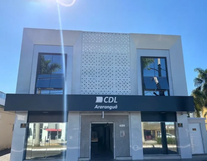 CDL Araranguá se posiciona contra novo feriado em SC Fachada frontal da sede da Câmara de Dirigentes Lojistas (CDL) de Araranguá, em Santa Catarina. O prédio de arquitetura moderna apresenta janelas espelhadas e uma placa preta centralizada com o logotipo da entidade em letras brancas. A imagem ilustra a instituição que lidera o movimento de preocupação com os impactos econômicos do novo projeto de lei estadual.