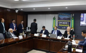 CPI aprova convite para Eduardo Leite depor sobre rodovias Registro fotográfico da reunião da CPI dos Contratos de Concessão das Rodovias Estaduais na Assembleia Legislativa do RS. Deputados estão sentados ao redor de uma mesa de madeira em formato de "U", debatendo. Ao fundo, vê-se um banner azul com os dizeres "CPI DOS PEDÁGIOS" e as bandeiras do Brasil e do Rio Grande do Sul. A imagem ilustra o momento em que a comissão aprovou o convite ao governador Eduardo Leite.