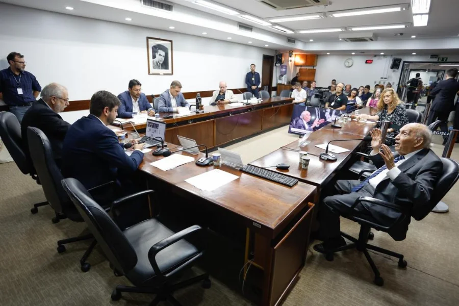 CPI das Rodovias debate custos e sistema Free Flow no RS Reunião da CPI dos Contratos de Concessão das Rodovias Estaduais na Assembleia Legislativa do Rio Grande do Sul. O conselheiro do DAER, Luís Roberto Ponte, um homem idoso de terno e gravata, gesticula com as mãos enquanto presta depoimento aos deputados sentados ao redor de uma longa mesa de madeira em uma sala de comissões. Vários parlamentares e assessores observam, e uma tela ao fundo exibe uma imagem da reunião.