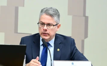 CPI ouve diretor da Meta sobre anúncios de crimes em redes Fotografia em plano médio do senador Alessandro Vieira, relator da CPI do Crime Organizado. Ele é um homem de pele clara, cabelos grisalhos e usa óculos de grau. Está vestido com um terno azul marinho e gravata azul, falando ao microfone durante uma sessão oficial no Senado Federal. À sua frente, há uma placa de identificação com seu nome.