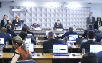 CPMI do INSS convoca Edson Araújo e Paulo Camisotti Vista ampla do plenário durante uma sessão da Comissão Parlamentar Mista de Inquérito (CPMI) que investiga fraudes no INSS. Ao fundo, uma mesa diretora com o senador Carlos Viana presidindo os trabalhos ao microfone. No primeiro plano e nas laterais, diversos parlamentares e participantes estão sentados em fileiras de mesas com notebooks abertos, acompanhando a reunião no Senado Federal.