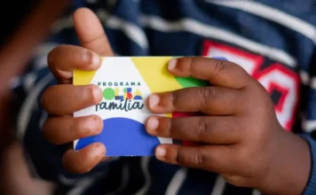 Caixa paga parcela de fevereiro do Bolsa Família para NIS 3 Mãos de uma criança seguram um cartão colorido do Programa Bolsa Família.