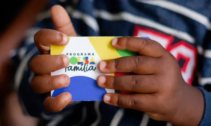 Caixa paga parcela de fevereiro do Bolsa Família para NIS 3 Mãos de uma criança seguram um cartão colorido do Programa Bolsa Família.