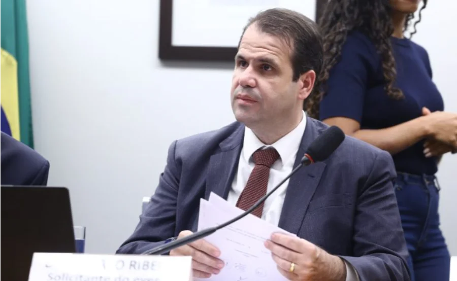 Deputado Aureo Ribeiro, proponente da lei que visa tornar crime hediondo a adulteração de produtos de tabaco em casos graves, manuseia papéis durante uma sessão legislativa na Câmara. A imagem ilustra o trabalho parlamentar por trás do projeto de combate ao mercado ilegal de cigarros.