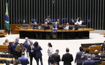 Câmara aprova criação da Agência Nacional de Proteção de Dados A imagem mostra uma vista geral do Plenário da Câmara dos Deputados durante uma sessão de votação. No centro da composição, a mesa diretora é ocupada por parlamentares, com o painel eletrônico de votação exibindo "00:00". No primeiro plano, diversos deputados e servidores conversam e se movimentam pelo plenário. A cena retrata o ambiente onde foi aprovada a Medida Provisória 1317/25, que cria a Agência Nacional de Proteção de Dados (AGPD), tema central da matéria.
