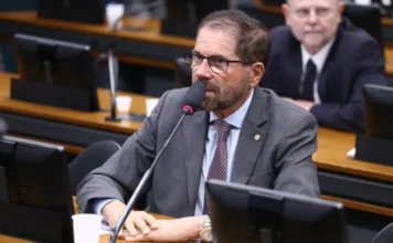Câmara aprova plano para reforçar segurança nas fronteiras O deputado federal José Rocha (União-BA), relator do projeto, aparece sentado à mesa de uma comissão na Câmara dos Deputados. Ele é um homem de pele clara, com barba e cabelos castanhos curtos, usa óculos de armação escura, terno cinza e gravata estampada. Ele fala ao microfone em um ambiente legislativo, com monitores e outras autoridades ao fundo em uma composição desfocada.