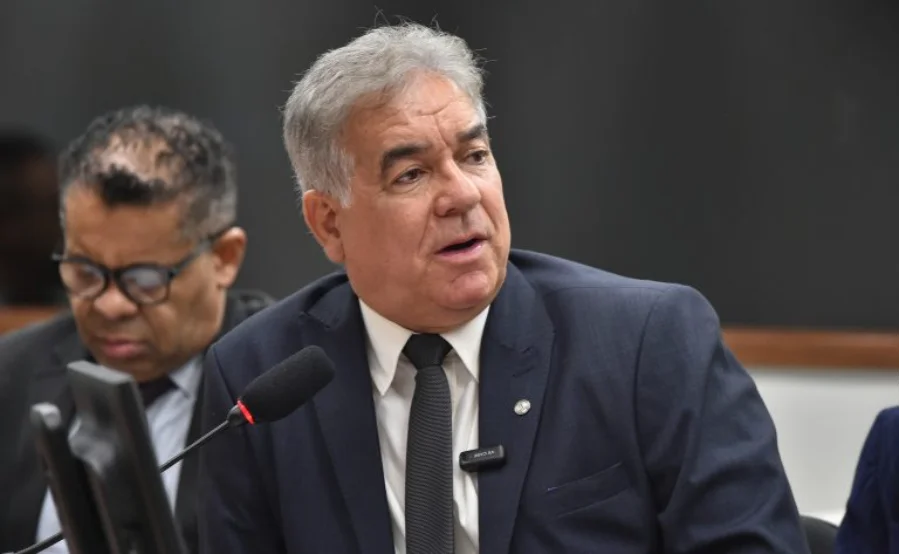 Fotografia em plano médio do deputado federal Zé Neto, autor do Projeto de Lei 1452/25, falando ao microfone durante uma sessão deliberativa na Câmara dos Deputados. O parlamentar, que veste terno azul-marinho e gravata escura, é o proponente da medida que visa permitir o uso de veículos com câmbio automático e elétricos nas aulas práticas de direção, visando uma frota mais sustentável e moderna.