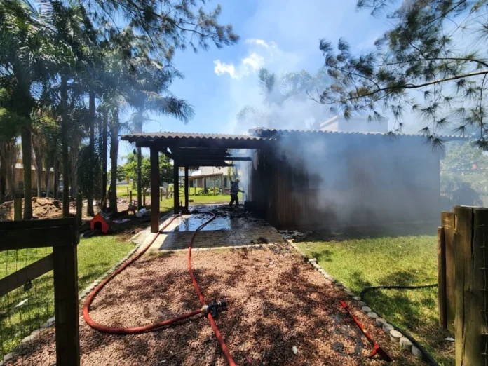 Campanha arrecada fraldas e roupas após incêndio em Sombrio Registro do local do incêndio que destruiu uma residência de madeira no bairro Januária, em Sombrio. A imagem mostra a atuação de um bombeiro e a fumaça saindo da estrutura, evidenciando o incidente que resultou na perda total dos bens da família, que agora solicita doações de fraldas e roupas.