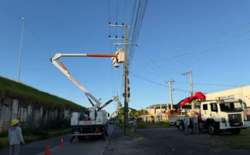Cersul reforça rede elétrica para escola em Araranguá Equipes técnicas e caminhões da Cersul, incluindo um com cesto aéreo, realizam trabalhos de reforço na rede elétrica em postes de energia na beira de uma estrada, obra necessária para atender a nova demanda da escola em Araranguá.