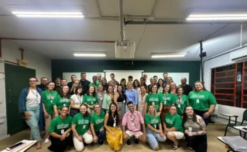 Colégio Unesc debate inovação e protagonismo estudantil Fotografia em grupo reúne dezenas de professores e gestores do Colégio Unesc em uma sala de aula durante a formação continuada. Os profissionais estão sorridentes, alguns em pé e outros agachados à frente, muitos utilizando uma camiseta verde padronizada do colégio. O ambiente escolar é iluminado e conta com lousa e projetor ao fundo, simbolizando o momento de integração e planejamento pedagógico.