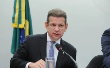 Comissão aprova lei de apoio a idosos com autismo Fotografia em plano médio do deputado Castro Neto, vestindo terno escuro e gravata azul, falando ao microfone durante uma sessão parlamentar. O deputado, que é o relator do projeto de lei sobre idosos com autismo, está sentado à mesa de comissões da Câmara dos Deputados. Ao fundo, à esquerda, é possível ver parte da bandeira do Brasil.