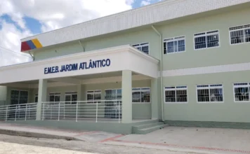 EJA em Arroio do Silva: Matrículas abertas até 13 de fevereiro Fotografia da fachada da Escola Municipal de Educação Básica Jardim Atlântico, em Balneário Arroio do Silva. O prédio de dois andares apresenta pintura em tons de verde claro e branco, com rampas de acessibilidade na entrada e uma placa azul com o nome da escola em destaque. O local é o ponto de atendimento noturno para as matrículas da EJA.