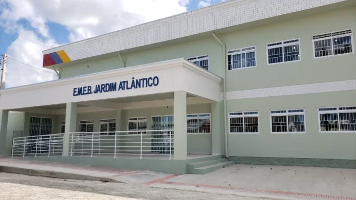 EJA em Arroio do Silva Matrículas abertas até 13 de fevereiro Fotografia da fachada da Escola Municipal de Educação Básica Jardim Atlântico, em Balneário Arroio do Silva. O prédio de dois andares apresenta pintura em tons de verde claro e branco, com rampas de acessibilidade na entrada e uma placa azul com o nome da escola em destaque. O local é o ponto de atendimento noturno para as matrículas da EJA.