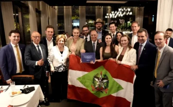 FIESC: Jornada de 40h pode extinguir 41 mil vagas em SC Fotografia mostra o presidente da FIESC, Gilberto Seleme, acompanhado por membros da bancada parlamentar de Santa Catarina em Brasília. O grupo está reunido em um ambiente formal e posa segurando a bandeira do estado de Santa Catarina e o livreto azul do estudo intitulado "Impactos Econômicos da Redução da Jornada de Trabalho em Santa Catarina".