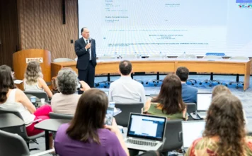 FIESC reúne 100 sindicatos para fortalecer a indústria O presidente da FIESC, Gilberto Seleme, discursa durante o workshop sindical para executivos na sede da Federação, em Florianópolis. A imagem mostra o auditório com participantes e uma tela ao fundo.