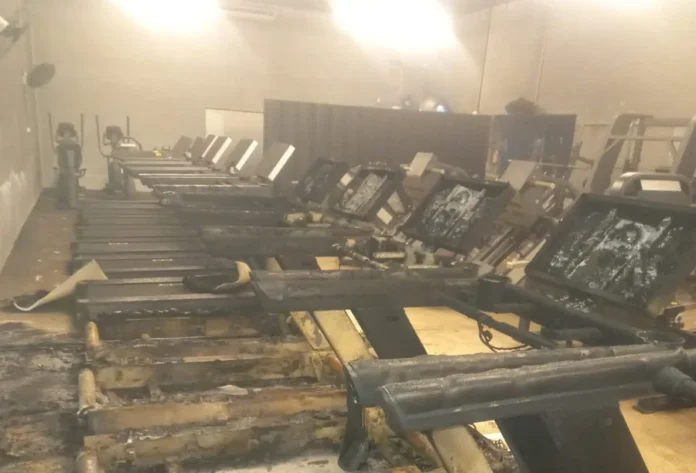 Fogo destrói equipamentos em academia no Centro de Içara Vista interna de uma academia no Centro de Içara após incêndio, exibindo uma fileira de esteiras de corrida com painéis e estruturas severamente danificados pelas chamas e pelo calor.