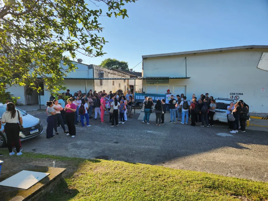 Funcionários do Hospital Santa Catarina entram em greve Foto externa mostra um grupo de dezenas de trabalhadores do Hospital Materno Infantil Santa Catarina, em Criciúma, reunidos no pátio lateral da instituição durante a manhã de quinta-feira. Eles estão de pé, a maioria mulheres, e seguram uma faixa horizontal azul com a frase