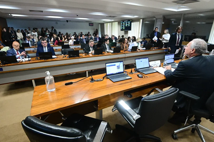 Vista geral da sala de sessões da Comissão de Assuntos Econômicos (CAE) do Senado Federal durante uma reunião. Em primeiro plano, um senador preside a mesa de costas para a câmera, enquanto outros parlamentares estão sentados à frente, no contexto das discussões do grupo de trabalho sobre o Banco Master.