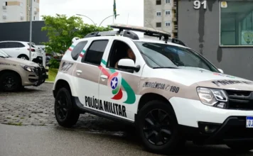 Hidrômetro é furtado de centro educacional em Criciúma Viatura da Polícia Militar de Santa Catarina (PMSC), modelo SUV de cor branca com grafismos em bege, verde e vermelho, estacionada em uma rua pavimentada. No detalhe lateral, lê-se "Polícia Militar" e o número de emergência "190". O dia está nublado e o pavimento parece úmido. Ao fundo, veem-se prédios e vegetação urbana.
