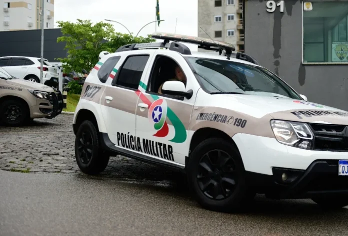 Hidrômetro é furtado de centro educacional em Criciúma Viatura da Polícia Militar de Santa Catarina (PMSC), modelo SUV de cor branca com grafismos em bege, verde e vermelho, estacionada em uma rua pavimentada. No detalhe lateral, lê-se "Polícia Militar" e o número de emergência "190". O dia está nublado e o pavimento parece úmido. Ao fundo, veem-se prédios e vegetação urbana.