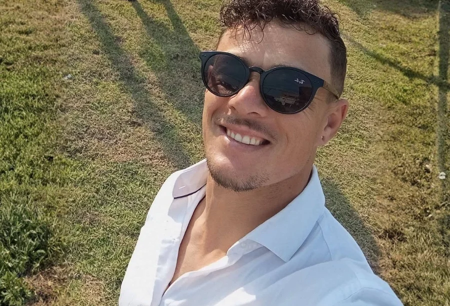 Retrato de Jonatan Pereira, 33 anos, vítima do afogamento no Rio Araranguá. Ele aparece sorrindo, usando óculos escuros e camisa branca em uma área externa gramada.