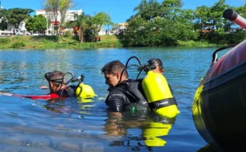 Homem morre afogado ao tentar atravessar o Rio Araranguá Dois mergulhadores do Corpo de Bombeiros, equipados com cilindros de oxigênio amarelos, realizam buscas subaquáticas nas águas do Rio Araranguá. Ao fundo, vê-se a margem arborizada e algumas pessoas observando.