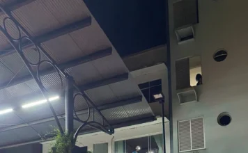 Homem morre após choque elétrico no Centro de Araranguá Fotografia noturna da área externa na Praça Hercílio Luz, em Araranguá, destacando em primeiro plano uma grande marquise de estrutura metálica. Ao fundo, é possível observar profissionais de emergência e técnicos trabalhando em um andar elevado de um edifício comercial, iluminados por lanternas e luzes da rua, durante o atendimento da ocorrência de choque elétrico.