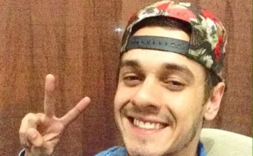 Identificado ciclista morto em acidente na BR-101 em Sombrio Fotografia de rosto de Marcos Vinicius Neumann Araujo Coelho, o ciclista de 28 anos que faleceu no acidente em Sombrio. Ele aparece sorrindo para a câmera, usando um boné estampado virado para trás e fazendo o sinal de paz com os dedos da mão direita.